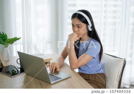 A focused Asian woman wearing headphones, listening to music while working on her laptop. A focused Asian woman wearing headphones, listening to music while working on her laptop. 107484338
