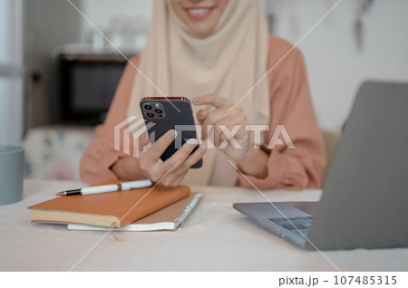 Close-up image of a Muslim woman is using her smartphone at a table in the kitchen 107485315