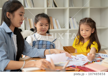 Two young Asian girls are enjoying studying English alphabet flashcards with a private teacher Two young Asian girls are enjoying studying English alphabet flashcards with a private teacher 107485658