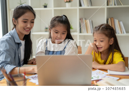 Two Asian girls are studying with a private teacher at home, learning a lesson on a laptop 107485685