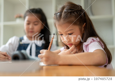 An adorable young Asian elementary school girl is focusing on studying, writing, or drawing 107485728