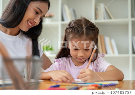A kind Asian female teacher or babysitter is babysitting and teaching art to a young girl 107485757