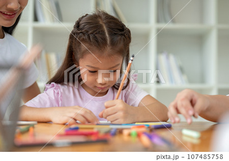 An adorable Asian elementary school girl is focusing on studying in the classroom with a teacher 107485758