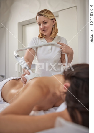 weight loss, Fighting overweight, anti cellulite massage. Young woman is taking part in beauty consultations, body shaping within professional beauty salon, masseur is using vacuum roller massage 107485814