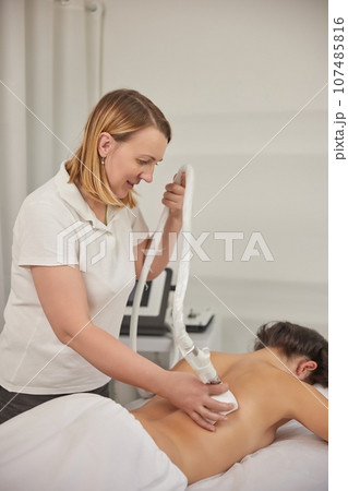 non-invasive method, LPG massage, beauty procedure. Young woman from beauty salon performs beauty services, body shaping, masseurs perform vacuum roller massages for clients, figure correcting non-invasive method, LPG massage, beauty procedure. Young woman from beauty salon performs beauty services, body shaping, masseurs perform vacuum roller massages for clients, figure correcting 107485816