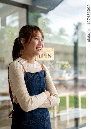 A pretty Asian female coffee shop owner standing with her arms crossed at the entrance door A pretty Asian female coffee shop owner standing with her arms crossed at the entrance door 107486000