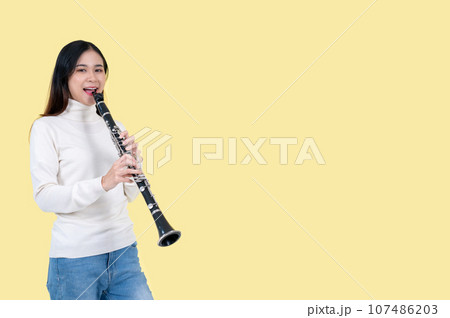 A beautiful and talented Asian woman playing a clarinet, isolated yellow background 107486203