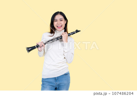 A beautiful and talented Asian woman holding a clarinet, isolated yellow background 107486204