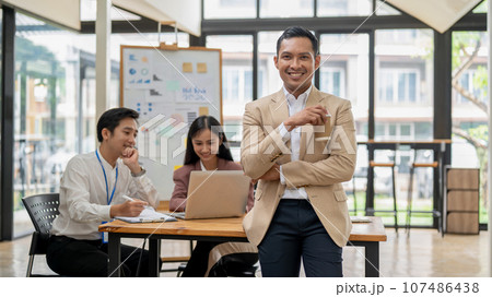 A handsome Asian male CEO stands with a coffee cup in his hand, smiling at the camera 107486438