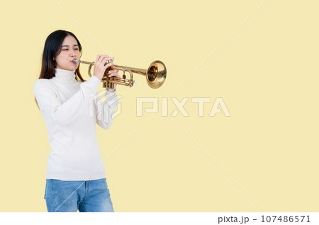 A pretty and talented Asian woman is playing the trumpet, isolated yellow background A pretty and talented Asian woman is playing the trumpet, isolated yellow background 107486571