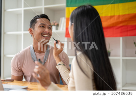 An attractive Asian gay man is being made up by a female makeup artist in his studio. 107486639