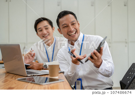 Two cheerful Asian male bankers or financial analysts are working together in the office. 107486674