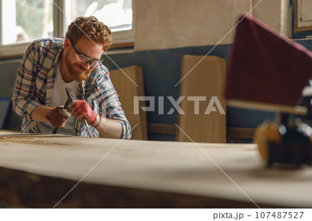 Professional craftsman working with chisel while cutting wooden plank in carpentry workshop Professional craftsman working with chisel while cutting wooden plank in carpentry workshop 107487527