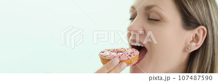 Happy woman bites delicious donut on light background 107487590