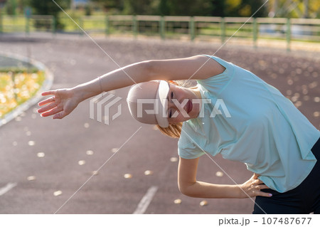 A young beautiful woman in sportswear plays sports at a local stadium. Exercise, jog and exercise at the beginning of the day. Healthy and active lifestyle. 107487677