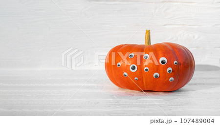 Pumpkin with Eyes for Halloween. Humor, Creative. One Big Orange Pumpkin with Many Eyes. Single Spooky Halloween Pumpkin, Jack O Lantern with Evil Face. White Wooden Textured Background. Front View 107489004