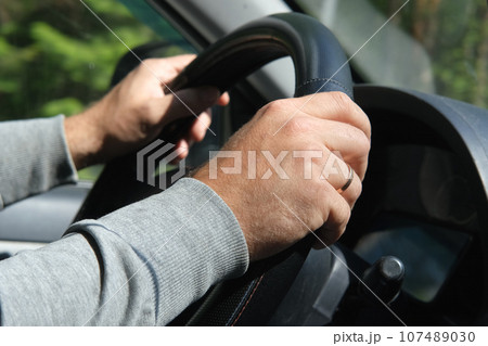 Male Hands holding steering wheel close up. Confident man driving a car during jorney trip. Side view from passenger inside car interior. Summer day. Driver. Selective Focus, Cropped. Travel concept Male Hands holding steering wheel close up. Confident man driving a car during jorney trip. Side view from passenger inside car interior. Summer day. Driver. Selective Focus, Cropped. Travel concept 107489030
