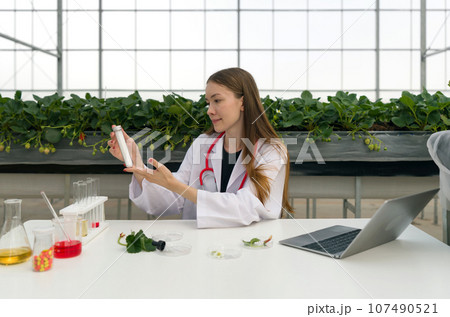 A scientist conducting research with a laptop within a vegetation-rich greenhouse. A scientist conducting research with a laptop within a vegetation-rich greenhouse. 107490521