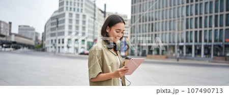 Asian girl walking on street, reading on tablet and drinking coffee outdoors Asian girl walking on street, reading on tablet and drinking coffee outdoors 107490713
