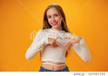 Friendly teen girl shows heart love gesture on yellow background Friendly teen girl shows heart love gesture on yellow background 107491185