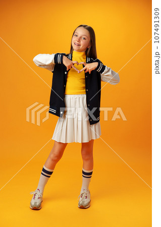Friendly teen girl shows heart love gesture on yellow background Friendly teen girl shows heart love gesture on yellow background 107491309