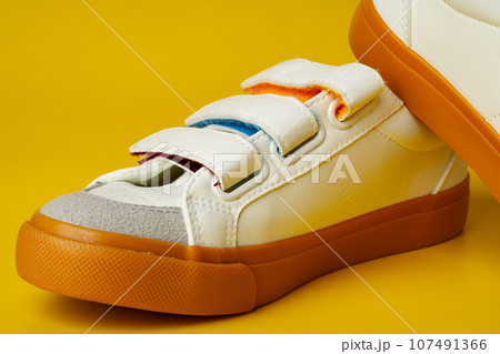 White leather sneakers with fasteners on yellow background 107491366