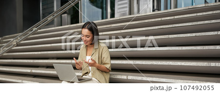 Vertical shot of asian girl student attend online meeting, talking at laptop, video chat, sitting on stairs Vertical shot of asian girl student attend online meeting, talking at laptop, video chat, sitting on stairs 107492055