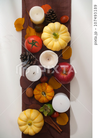 Frame of colorful autumn leaves with pumpkins, ripe tomatoes, dry pine cone and nuts on white and brown background. Creative scene for advertising with Thanksgiving concept Frame of colorful autumn leaves with pumpkins, ripe tomatoes, dry pine cone and nuts on white and brown background. Creative scene for advertising with Thanksgiving concept 107493189