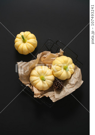 Mysterious black background with mini pumpkins placed on a black plastic basket. Decorative pumpkins for Thanksgiving. Scene for advertising, minimalist concept 107493241