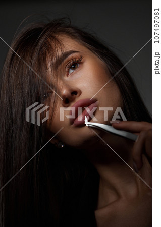 beautiful woman holding eyelashes tweezers on black background 107497081
