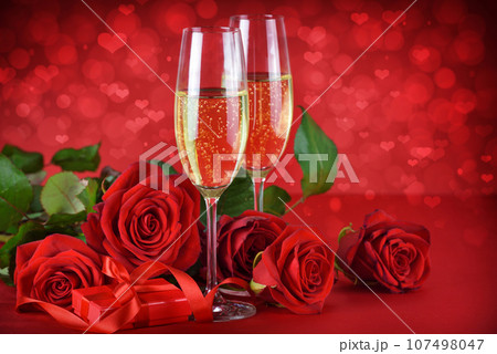 Romantic date night concept. Champagne, gift and roses on a festive red background with hearts. 107498047