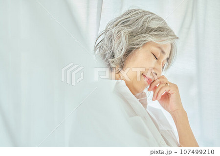白いカーテンに立つシニア女性 107499210