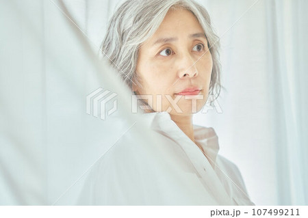 白いカーテンに立つシニア女性 107499211