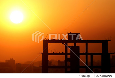 Setting sun behind construction building Setting sun behind construction building 107500899