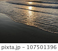 夕陽が映る海の波打ち際 107501396