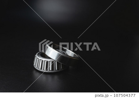 New angular contact roller bearing of a new hub close-up, auto parts on a black background New angular contact roller bearing of a new hub close-up, auto parts on a black background 107504377