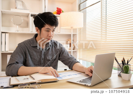 Man sat typing away on a laptop in his office with a determined look on his face, Work from the comfort of home, Male hand pressing on laptop keyboard, Work from home. 107504918