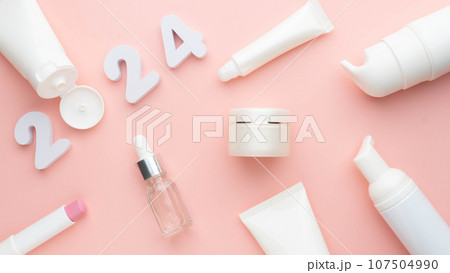 Best skincare products and cosmetic trends of 2024 concept. 2024 white number with lip balm, cream bottle, serum and lotion on pink background. 107504990