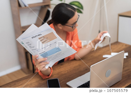 Female fills tax form holding current expense document in hands while sitting at workplace at home concentrated woman checks banking account score per month of stay 107505579