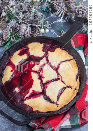 Homemade berry cobbler in cast iron skillet, Christmas decoration on background, vertical, top view 107508169