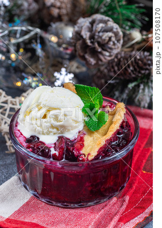 Berry cobbler in glass ramekin with ice cream, Christmas decoration, vertical 107508170