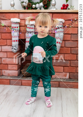 A little girl stands against the backdrop of a brick fireplace 107511233