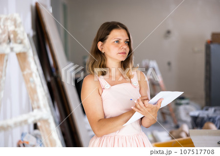 Woman designer checking documents during repair works 107517708