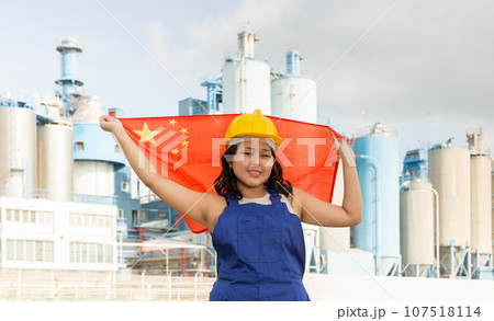 Happy asian girl in work clothes and hardhat with flag of china standing in front of industrial scenery Happy asian girl in work clothes and hardhat with flag of china standing in front of industrial scenery 107518114