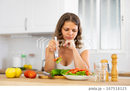 Portrait of displeased woman eating salad at home 107518125