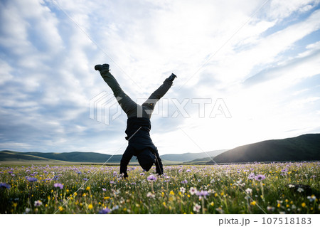 Woman hiker doing a handstand on high altitude mountain meadow Woman hiker doing a handstand on high altitude mountain meadow 107518183
