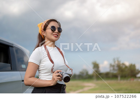 A positive Asian woman in sunglasses travels by car, arriving at her destination in the countryside. 107522266