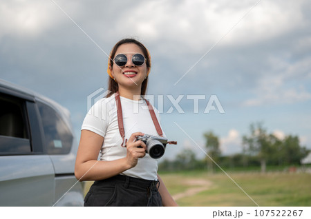 A positive Asian woman in sunglasses travels by car, arriving at her destination in the countryside. 107522267