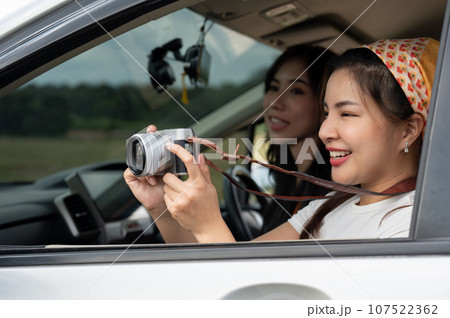 A cheerful Asian girl is taking pictures with her camera during her road trip with friends. 107522362