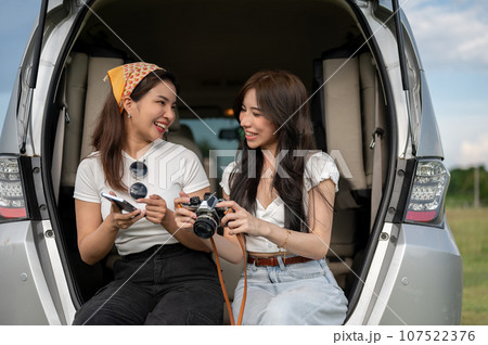 Two happy Asian female are checking the pictures on the camera, having fun during their road trip Two happy Asian female are checking the pictures on the camera, having fun during their road trip 107522376